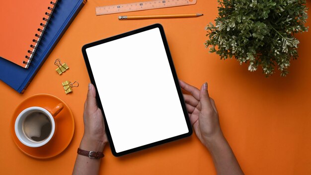 オレンジ色の背景に空の画面でモックアップデジタルタブレットを保持している若い女性デザイナー。