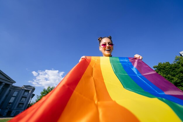 A young woman develops a rainbow flag against the sky