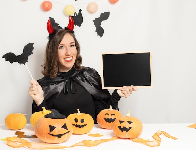 悪魔の衣装を着た若い女性が空の黒板を保持し、テキストのコピー スペース領域をオンライン マーケティング広告発表コンセプト