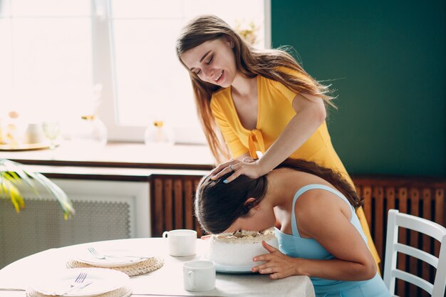 Young woman dips face in white cake with cream. Happy birthday concept.