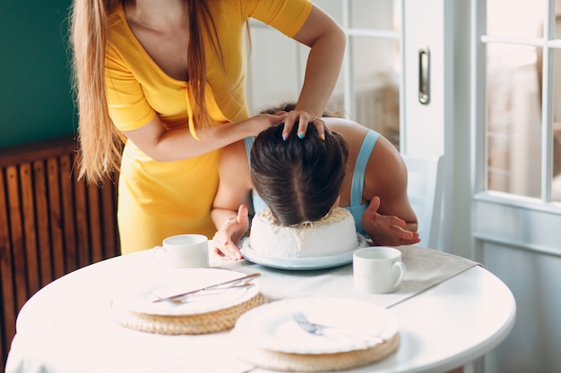 Young woman dips face in white cake with cream. Happy birthday concept.