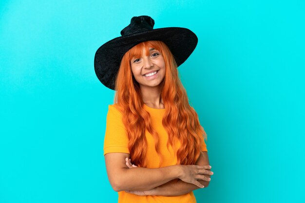 Young woman disguised as witch isolated on blue background with arms crossed and looking forward