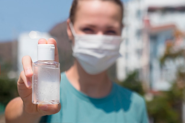 Young woman disinfects hands, girl in protective medical mask on face show bottle with sanitizer