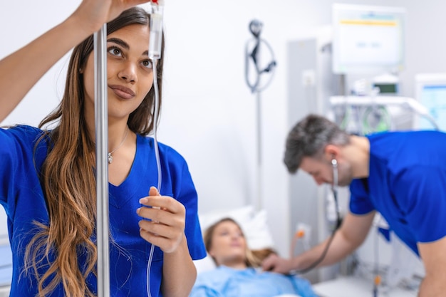 Young woman doctor anesthesiologist dressed in blue gown puts the IV dropper in hospital room