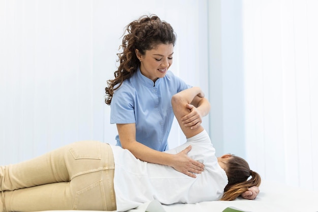 Young woman doctor chiropractor or osteopath fixing lying\
womans back with hands movements during visit in manual therapy\
clinic professional chiropractor during work