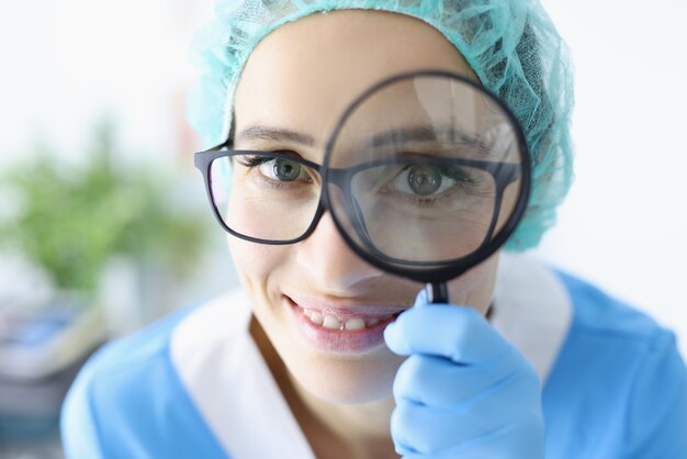 Foto medico della giovane donna in vetri che tengono lente d'ingrandimento