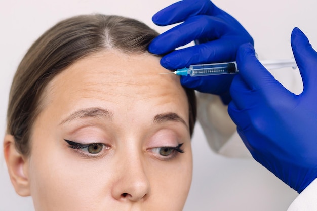 Young woman and doctor hands in blue gloves holding syringe needle for injection of facial wrinkles