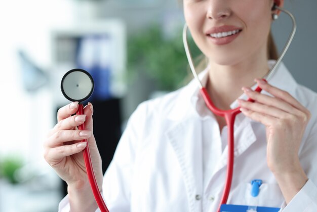 Young woman doctor holding red stethoscope in clinic closeup