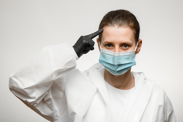 Young woman doctor in medical mask which points finger at her head.