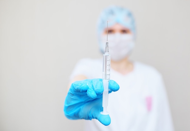 A young woman doctor or nurse in a medical mask holding a syringe with an injection or medication with a drop on the end of the needle close-up.copy space, text space