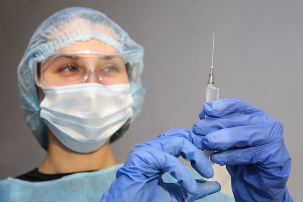 young woman doctor nurse in a protective mask with a syringe in her hand