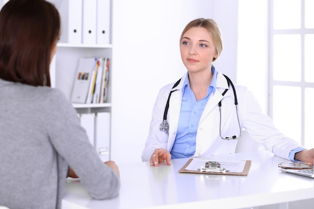 Young woman doctor and patient at medical examination at hospital office. Blue color blouse of therapist looks good. Medicine and healthcare concept.