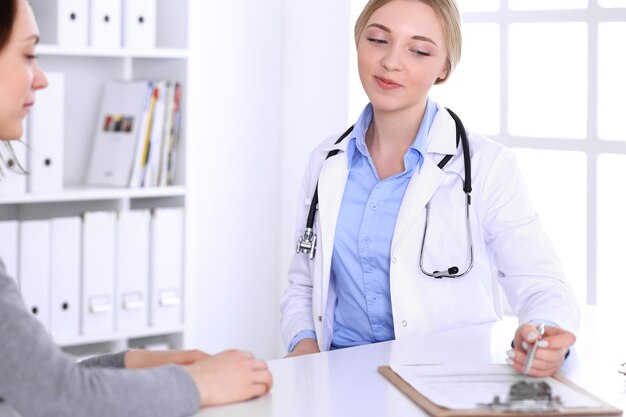 Young woman doctor and patient at medical examination at hospital office. Blue color blouse of therapist looks good. Medicine and healthcare concept.