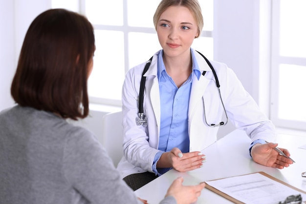 Young woman doctor and patient at medical examination at hospital office. Blue color blouse of therapist looks good. Medicine and healthcare concept.
