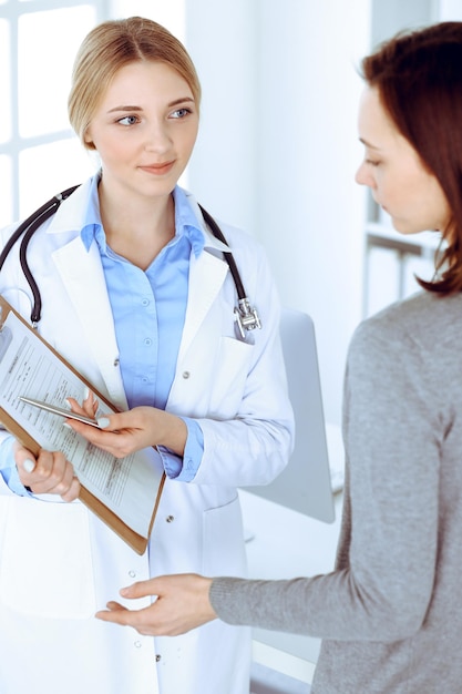 Young woman doctor and patient at medical examination at hospital office. Blue color blouse of therapist looks good. Medicine and healthcare concept.