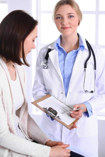 Young woman doctor and patient at medical examination at hospital office. Blue color blouse of therapist looks good. Medicine and healthcare concept.