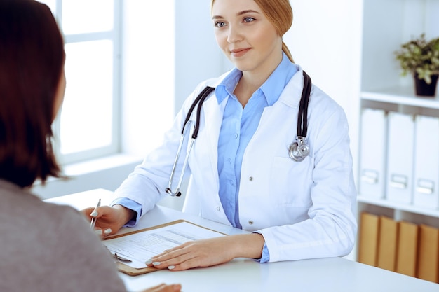 Young woman doctor and patient at medical examination in hospital office. Khaki colored blouse of therapist looks good. Medicine, healthcare and doctor's appointment concept.