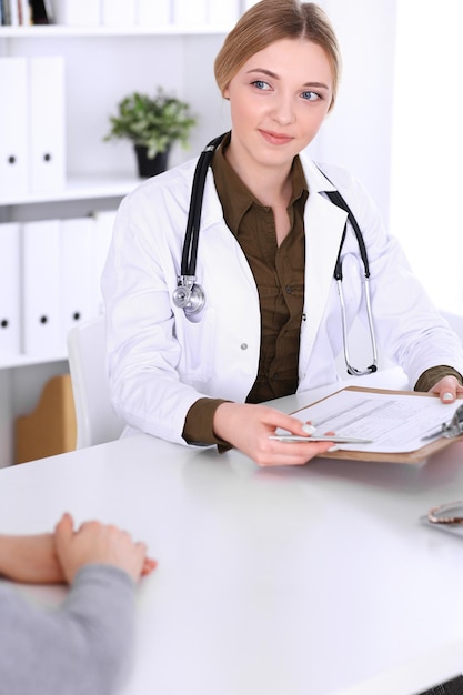 Young woman doctor and patient at medical examination in hospital office. Khaki colored blouse of therapist looks good. Medicine, healthcare and doctor's appointment concept.