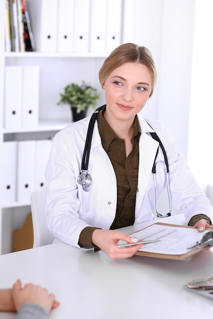 Young woman doctor and patient at medical examination in hospital office. Khaki colored blouse of therapist looks good. Medicine, healthcare and doctor's appointment concept.