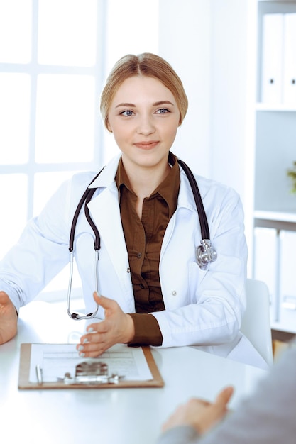 Photo young woman doctor and patient at medical examination in hospital office. khaki colored blouse of therapist looks good. medicine, healthcare and doctor's appointment concept.