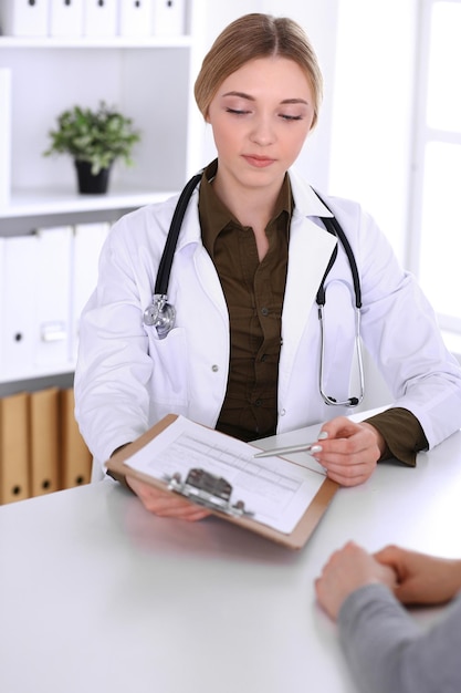 Young woman doctor and patient at medical examination in hospital office. Khaki colored blouse of therapist looks good. Medicine, healthcare and doctor's appointment concept.