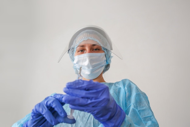 young woman doctor in a protective suit and mask with a syringe