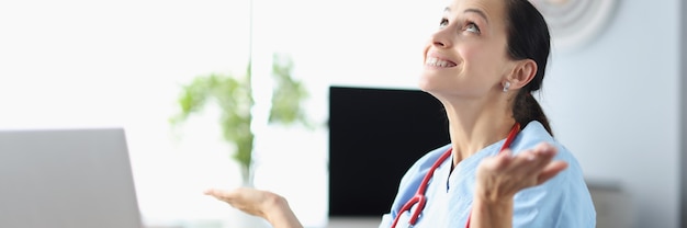 Young woman doctor sits at her work table and looks up