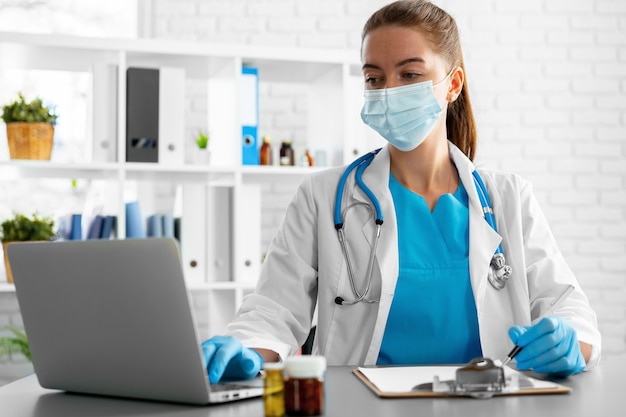 Young woman doctor sitting at working table using laptop close up