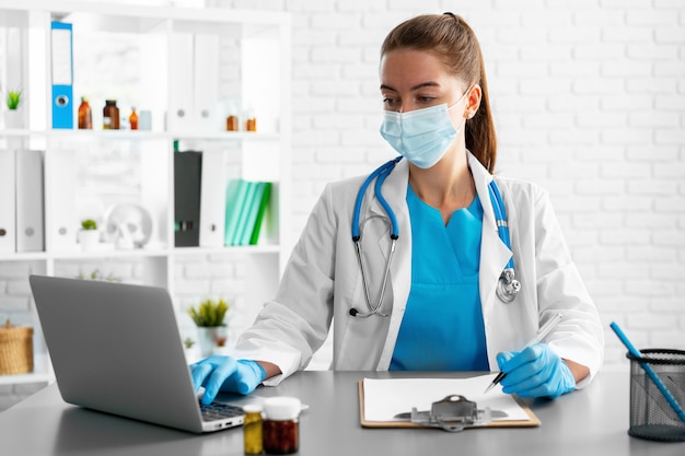 Young woman doctor sitting at working table using laptop close up