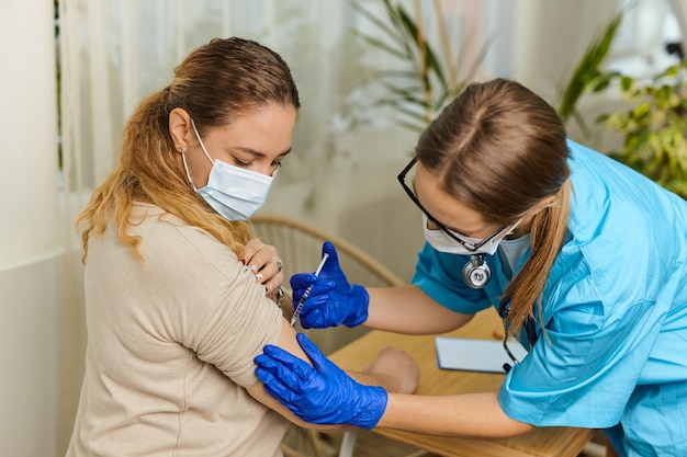 Young woman doctor vaccinates against coronavirus Covid 19 to a young woman in the office of a medical clinic