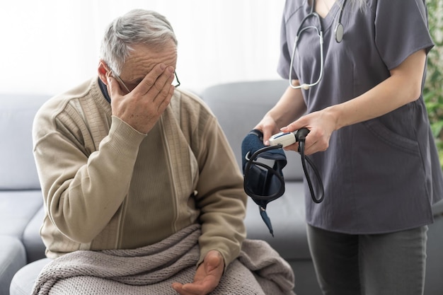 young woman doctor wearing white uniform with stethoscope checking mature patient blood pressure at