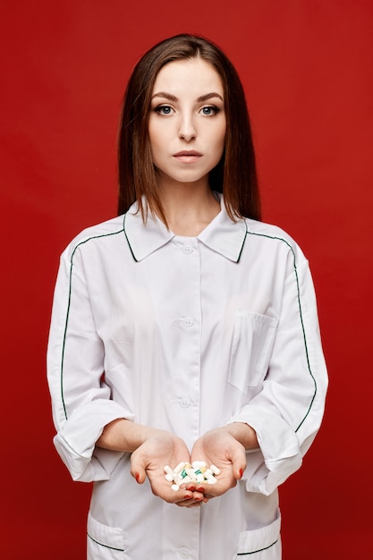 Young woman doctor in white medical coat holding pills in her open palms, copy space, isolated. Healthcare concept