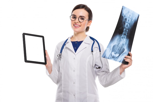 Young woman doctor with stethoscope looking at x-ray making diagnosis in white uniform on white 