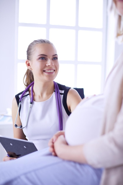 Young woman doctor with stethoscope and tablet speaking with pregnant woman at hospital