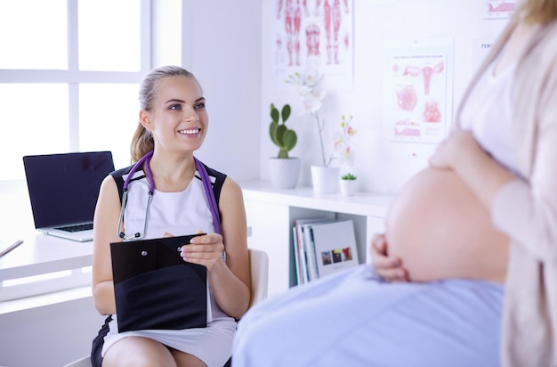 病院で妊娠中の女性と話す聴診器とタブレットを持つ若い女性医師