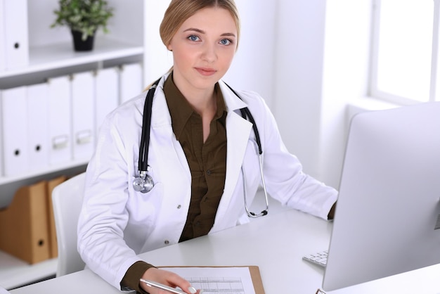 デスクトップPCモニターを見ている病院で働く若い女性医師。医師は投薬履歴の記録と検査結果を管理します。医学とヘルスケアの概念。