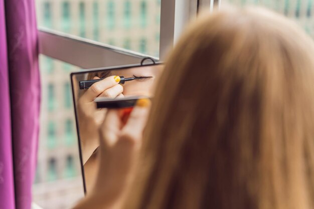 Young woman does makeup sitting by the window with a panoramic view of the skyscrapers and the big