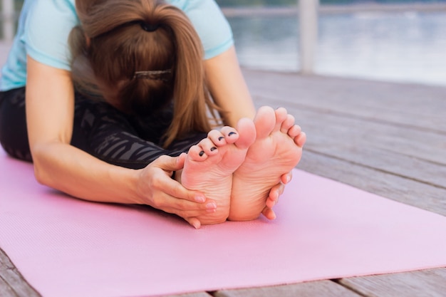 Young woman does yoga on a pink mat on a pier by the sea