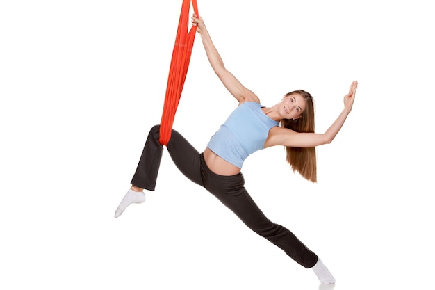 Young woman doing anti-gravity aerial yoga in red hammock on a seamless white wall