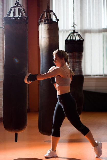 Young woman doing boxing workout in the gym she is wearing boxing gloves and punching a punching bag