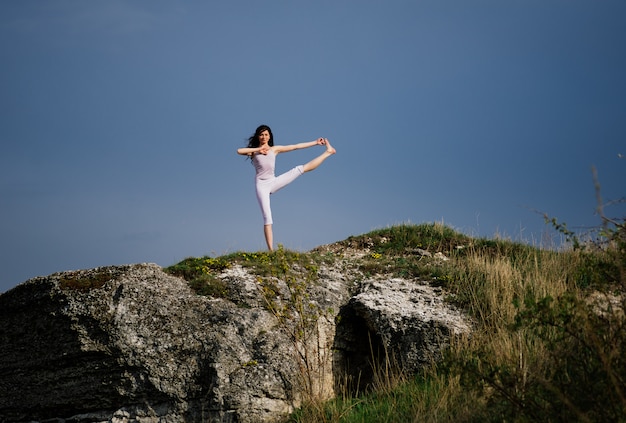 Foto giovane donna che fa esercizio complesso di yoga su una roccia