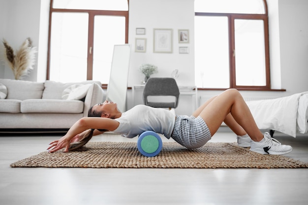 Young woman doing exercise with gymnastic roll on the floor at home