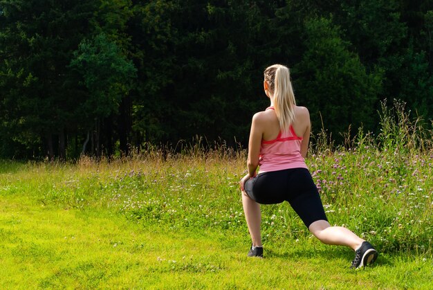 Giovane donna che fa esercizi di stretching all'aperto in un prato fuori città