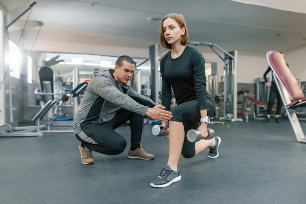 Young woman doing exercises with personal instructor in gym