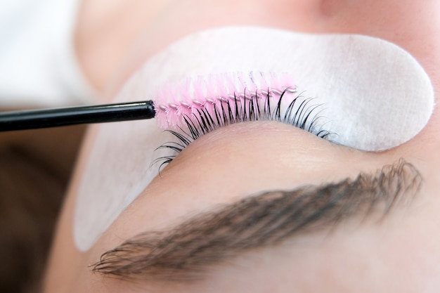 Young woman doing eyelash lamination procedure in a beauty salon, close-up