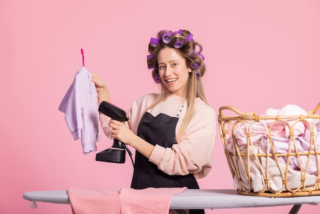 A young woman doing household chores irons childs sweatshirt hung on hanger using clothes steamer