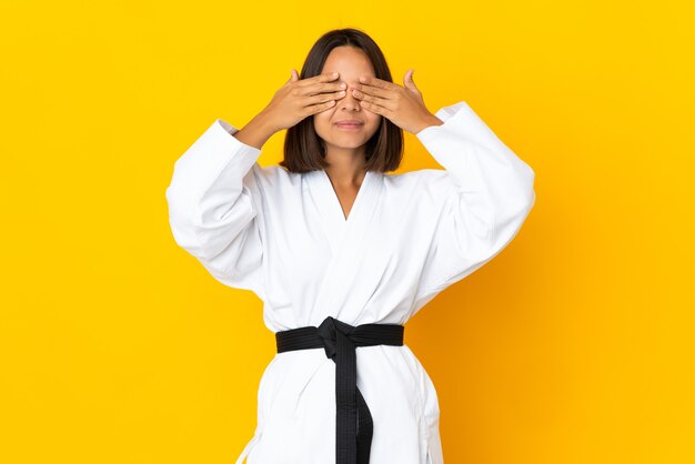 Young woman doing karate isolated on yellow background covering eyes by hands