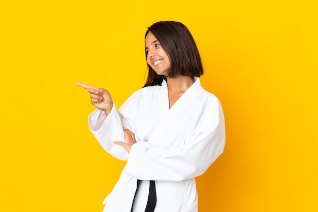 Young woman doing karate isolated on yellow background pointing finger to the side and presenting a product