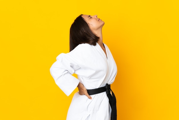 Young woman doing karate isolated on yellow background suffering from backache for having made an effort