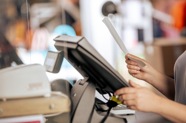 Young woman doing process payment with the bill or invoice on the pos cash terminal in the shop fina